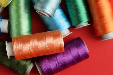 Photo of Different spools of sewing threads on red background, top view