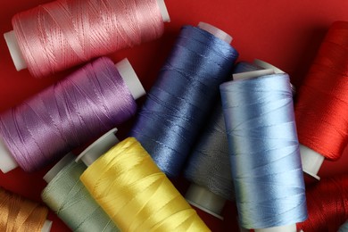 Photo of Different spools of sewing threads on red background, top view