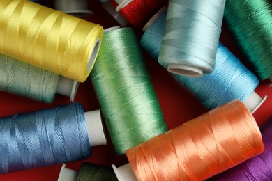 Photo of Different spools of sewing threads on red background, top view