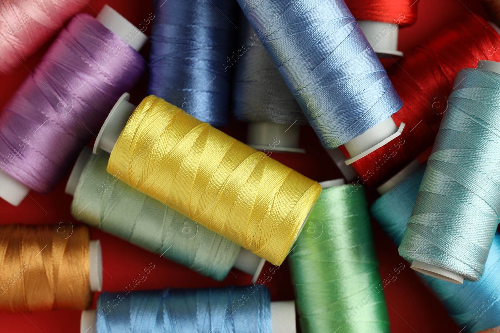 Photo of Different spools of sewing threads on red background, top view