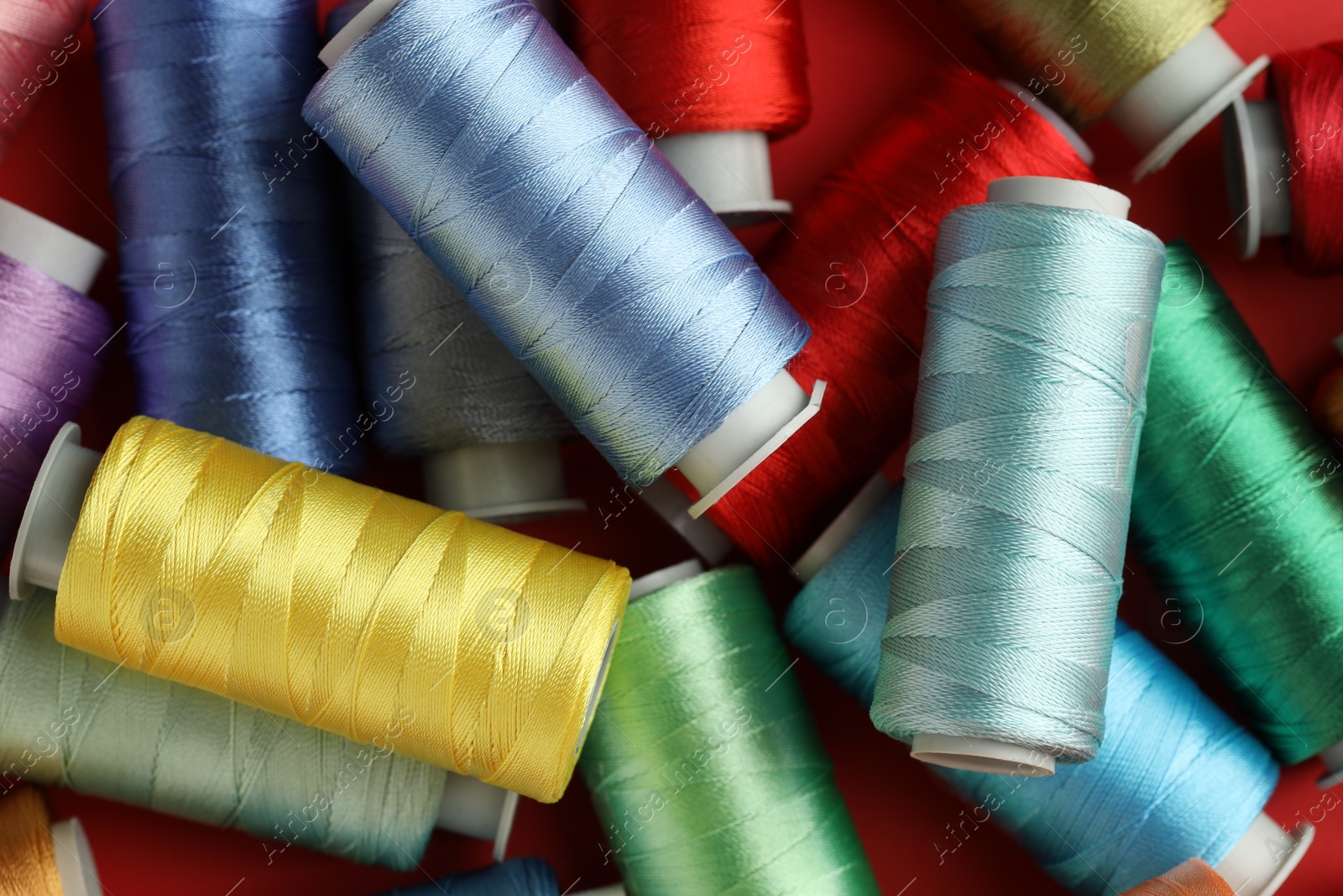 Photo of Different spools of sewing threads on red background, top view