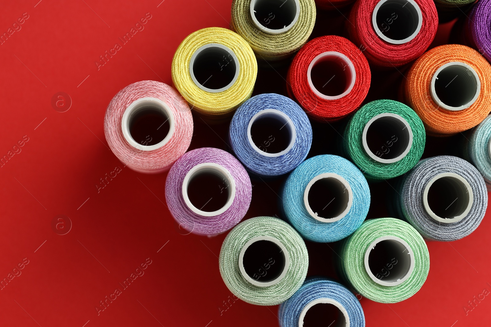 Photo of Different spools of sewing threads on red background, flat lay. Space for text