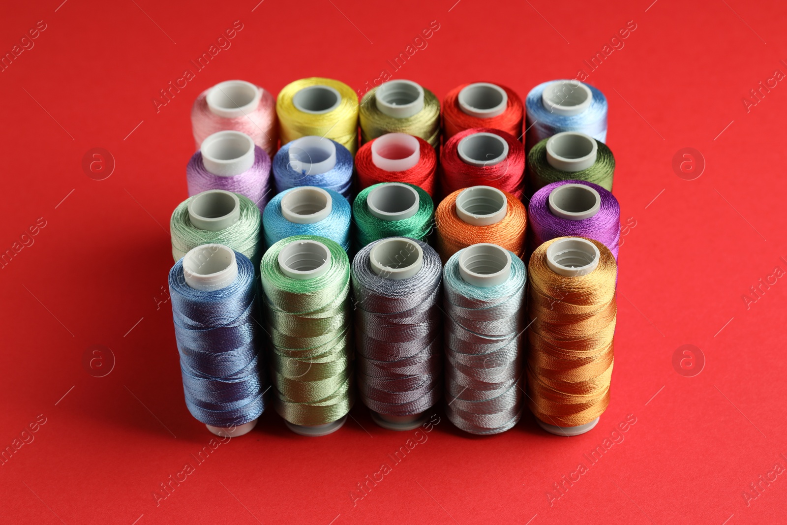 Photo of Different spools of sewing threads on red background, closeup