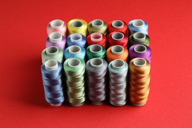 Photo of Different spools of sewing threads on red background, closeup