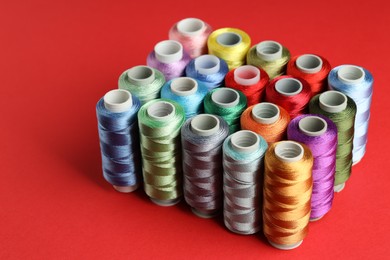 Photo of Different spools of sewing threads on red background, closeup. Space for text