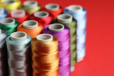 Photo of Different spools of sewing threads on red background, closeup