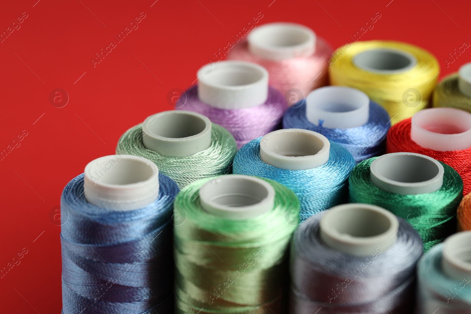 Photo of Different spools of sewing threads on red background, closeup