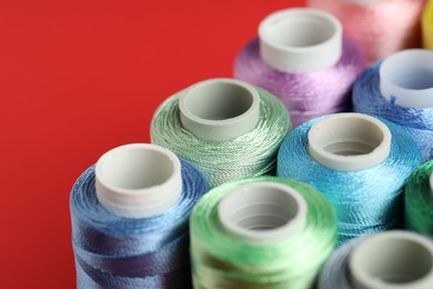 Photo of Different spools of sewing threads on red background, closeup