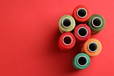 Photo of Different spools of sewing threads on red background, flat lay. Space for text