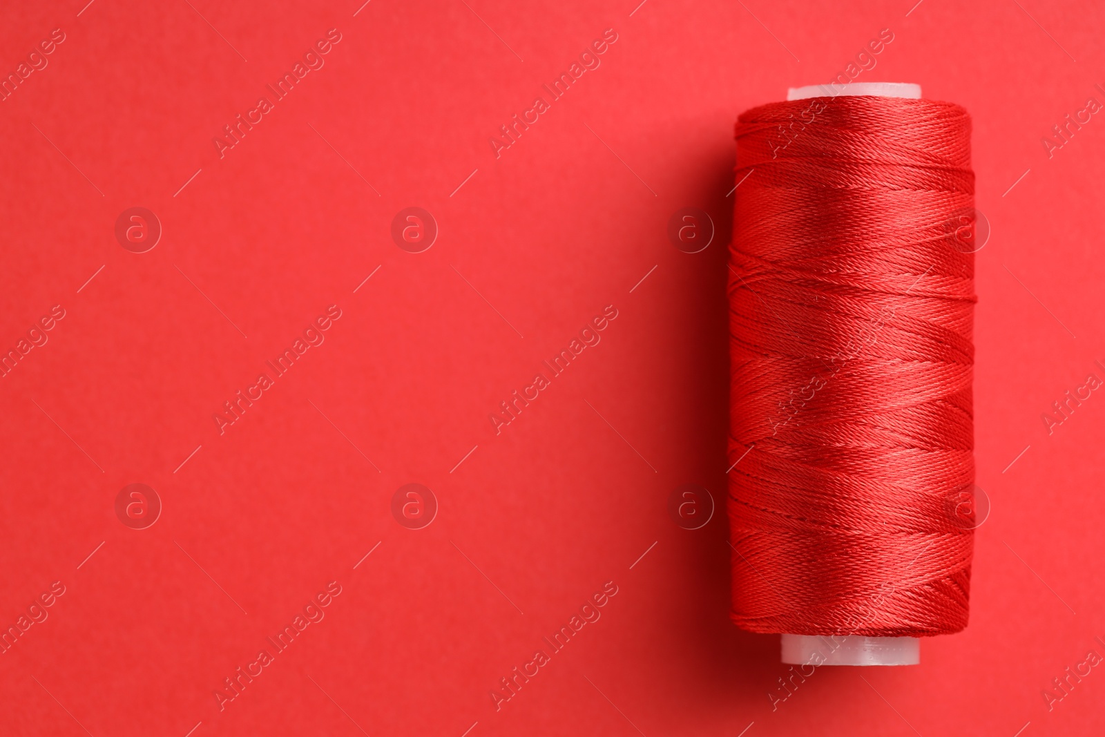 Photo of Spool of sewing thread on red background, top view. Space for text