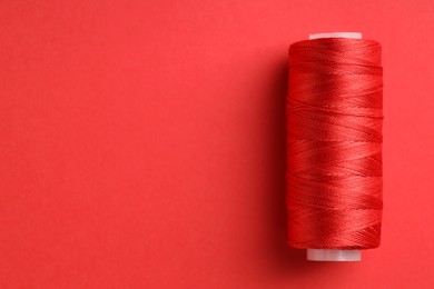 Photo of Spool of sewing thread on red background, top view. Space for text