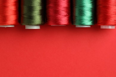 Photo of Different spools of sewing threads on red background, flat lay. Space for text