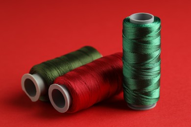 Photo of Different spools of sewing threads on red background, closeup