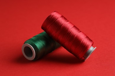 Photo of Different spools of sewing threads on red background, closeup