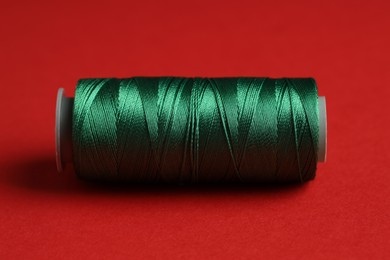 Photo of Spool of green sewing thread on red background, closeup