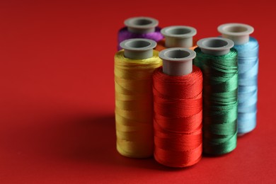 Photo of Different spools of sewing threads on red background, closeup. Space for text