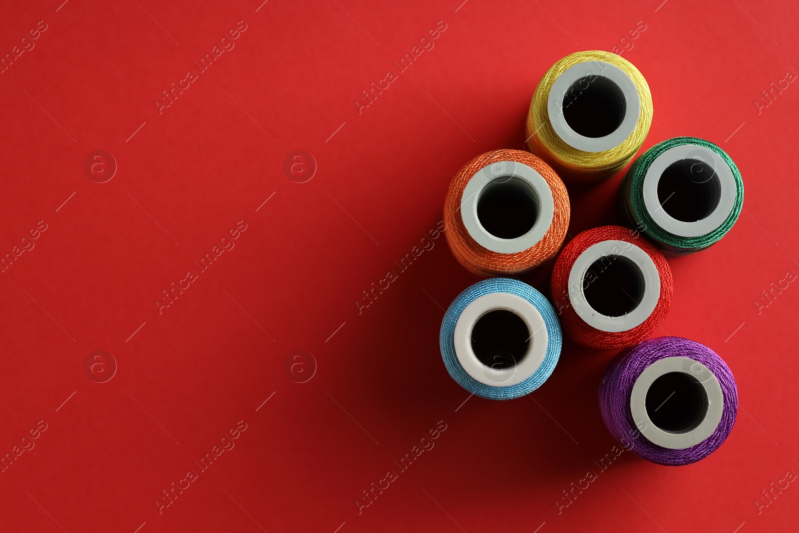 Photo of Different spools of sewing threads on red background, flat lay. Space for text