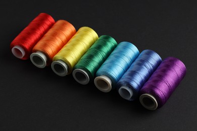 Photo of Different spools of sewing threads on black background, closeup