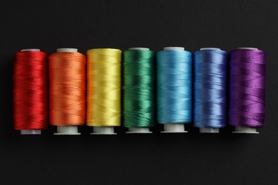 Photo of Different spools of sewing threads on black background, flat lay