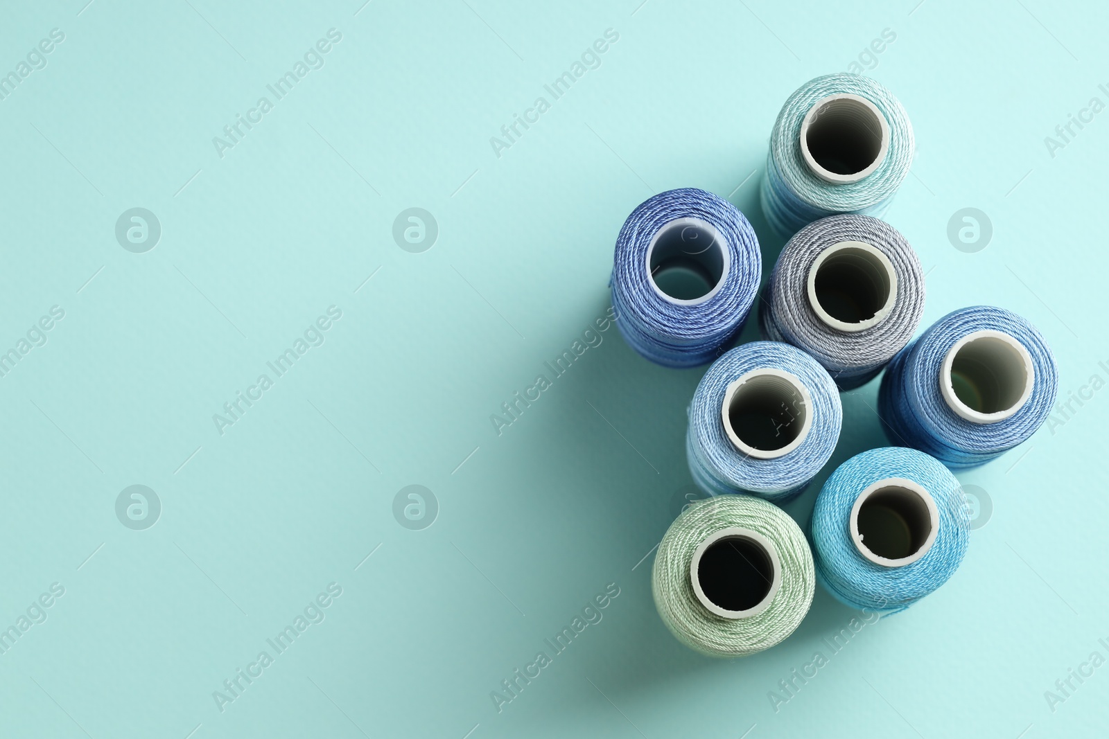 Photo of Different spools of sewing threads on light blue background, flat lay. Space for text