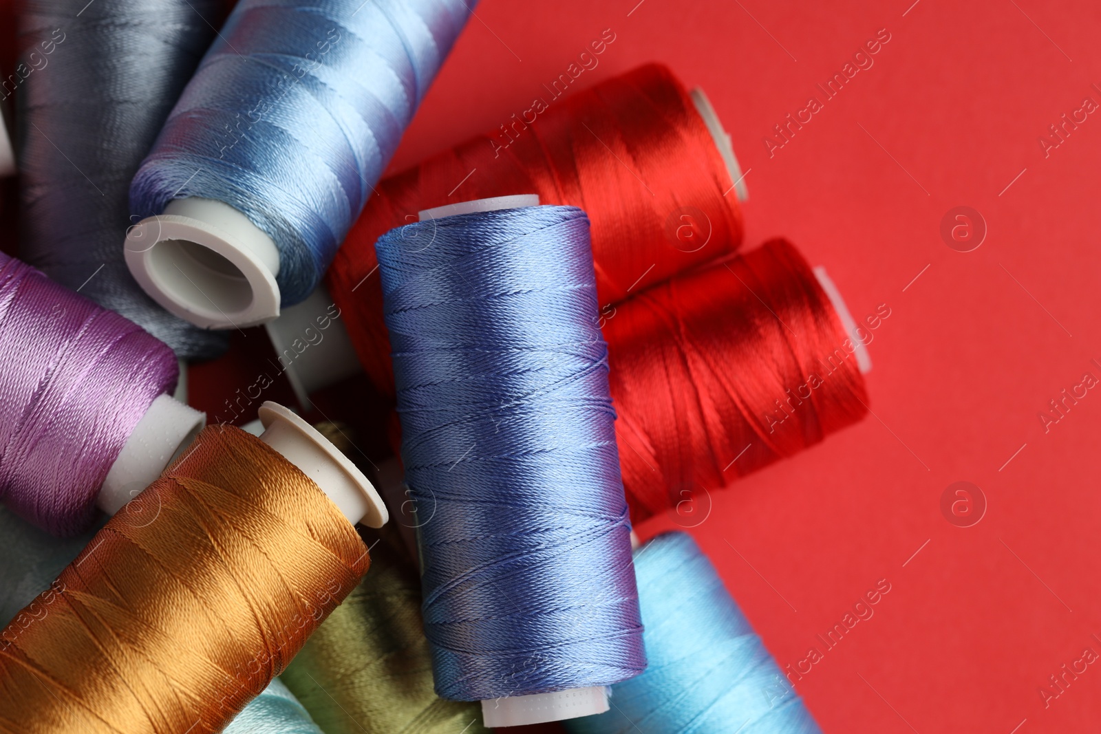 Photo of Different spools of sewing threads on red background, flat lay