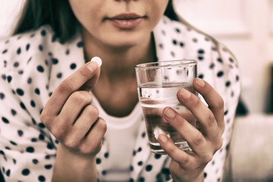 Image of Young woman taking pill indoors, closeup. Toned for dramatic atmosphere