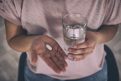 Young woman with pill and glass of water indoors, closeup. Toned for dramatic atmosphere