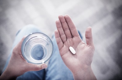 Image of Young woman with pill and glass of water indoors, top view. Toned for dramatic atmosphere