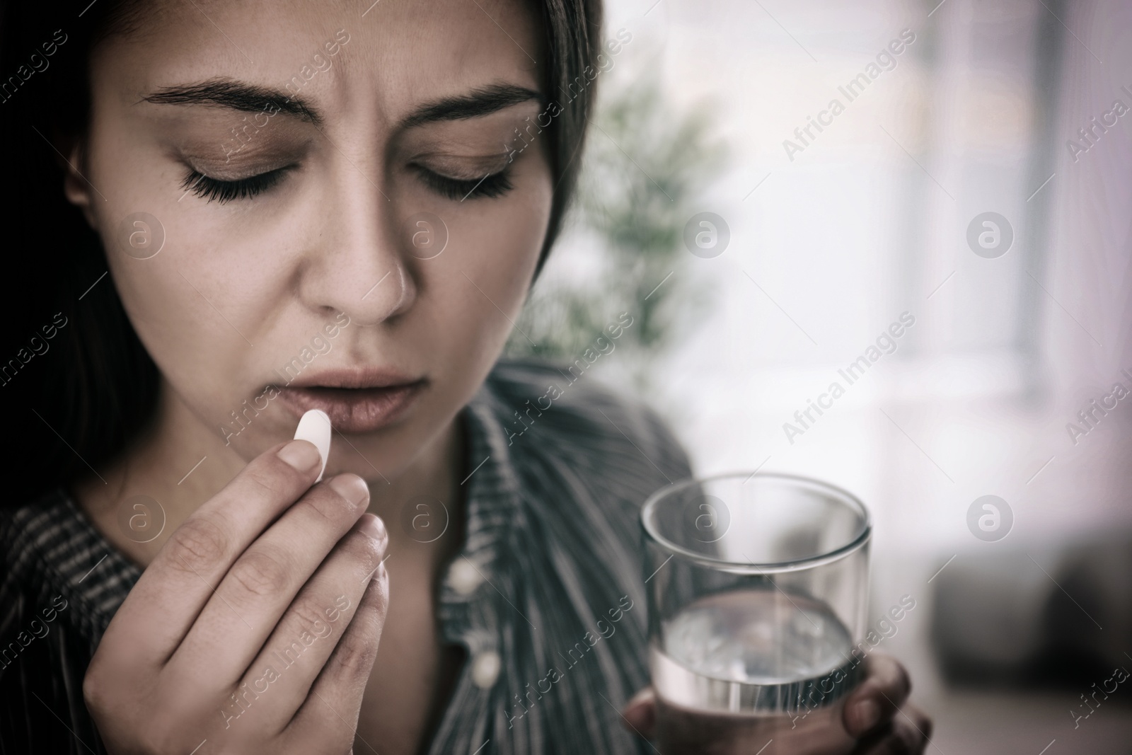 Image of Sad young woman taking pill indoors, closeup. Toned for dramatic atmosphere