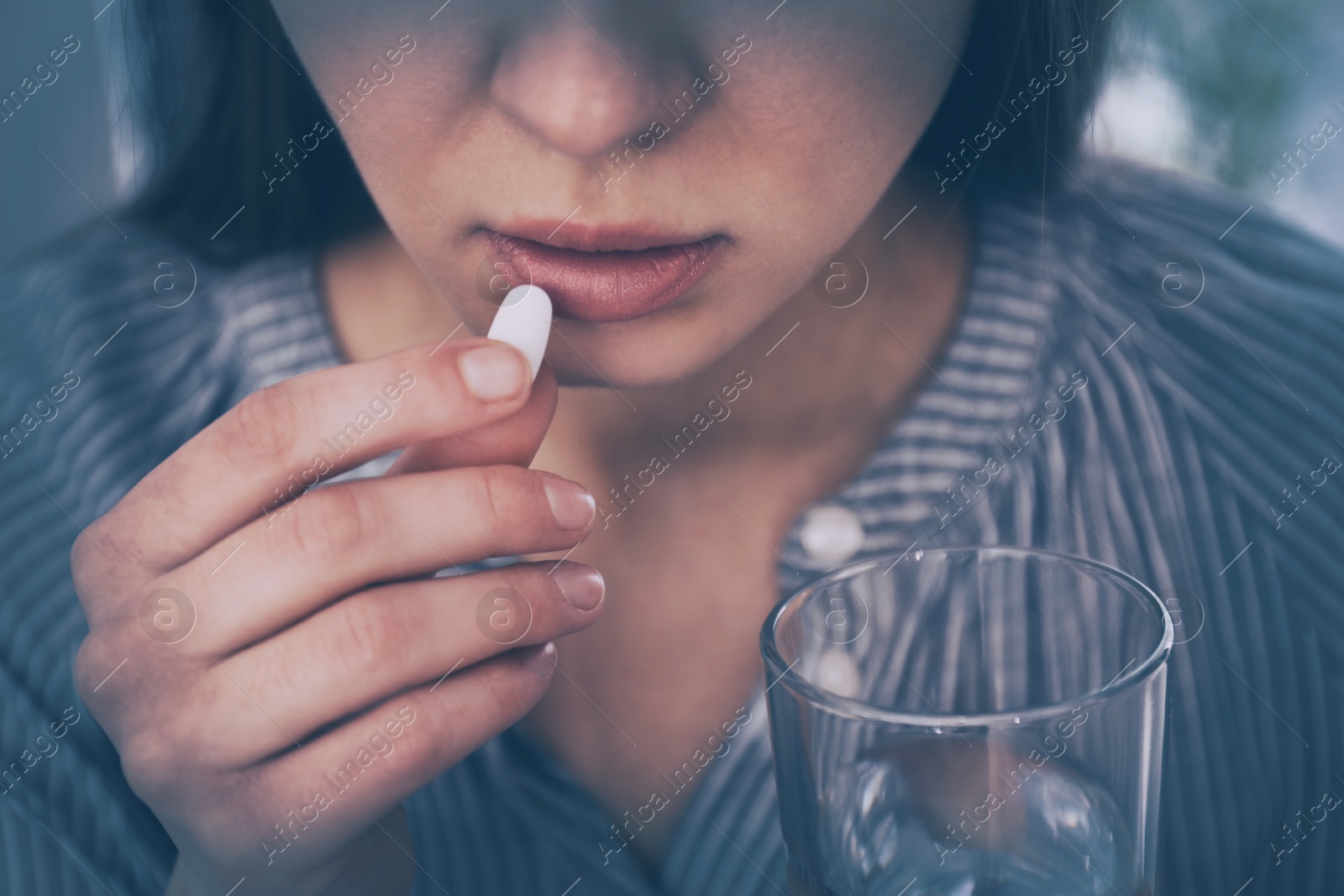 Image of Young woman taking pill indoors, closeup. Toned for dramatic atmosphere