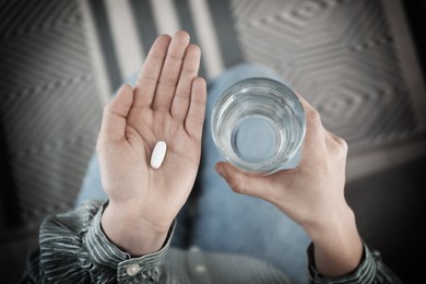 Young woman with pill and glass of water indoors, top view. Toned for dramatic atmosphere