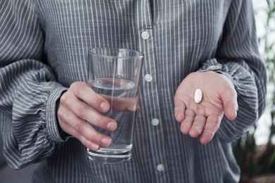 Young woman with pill and glass of water indoors, closeup. Toned for dramatic atmosphere