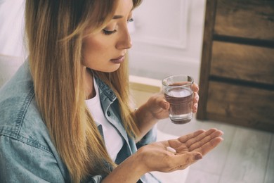 Image of Sad young woman taking pill indoors, closeup. Toned for dramatic atmosphere