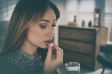 Image of Sad young woman taking pill indoors, closeup. Toned for dramatic atmosphere