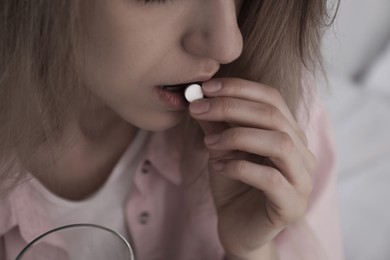 Image of Young woman taking pill indoors, closeup. Toned for dramatic atmosphere