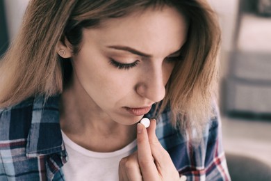 Sad young woman taking pill indoors, closeup. Toned for dramatic atmosphere