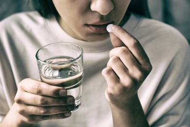 Image of Young woman taking pill indoors, closeup. Toned for dramatic atmosphere