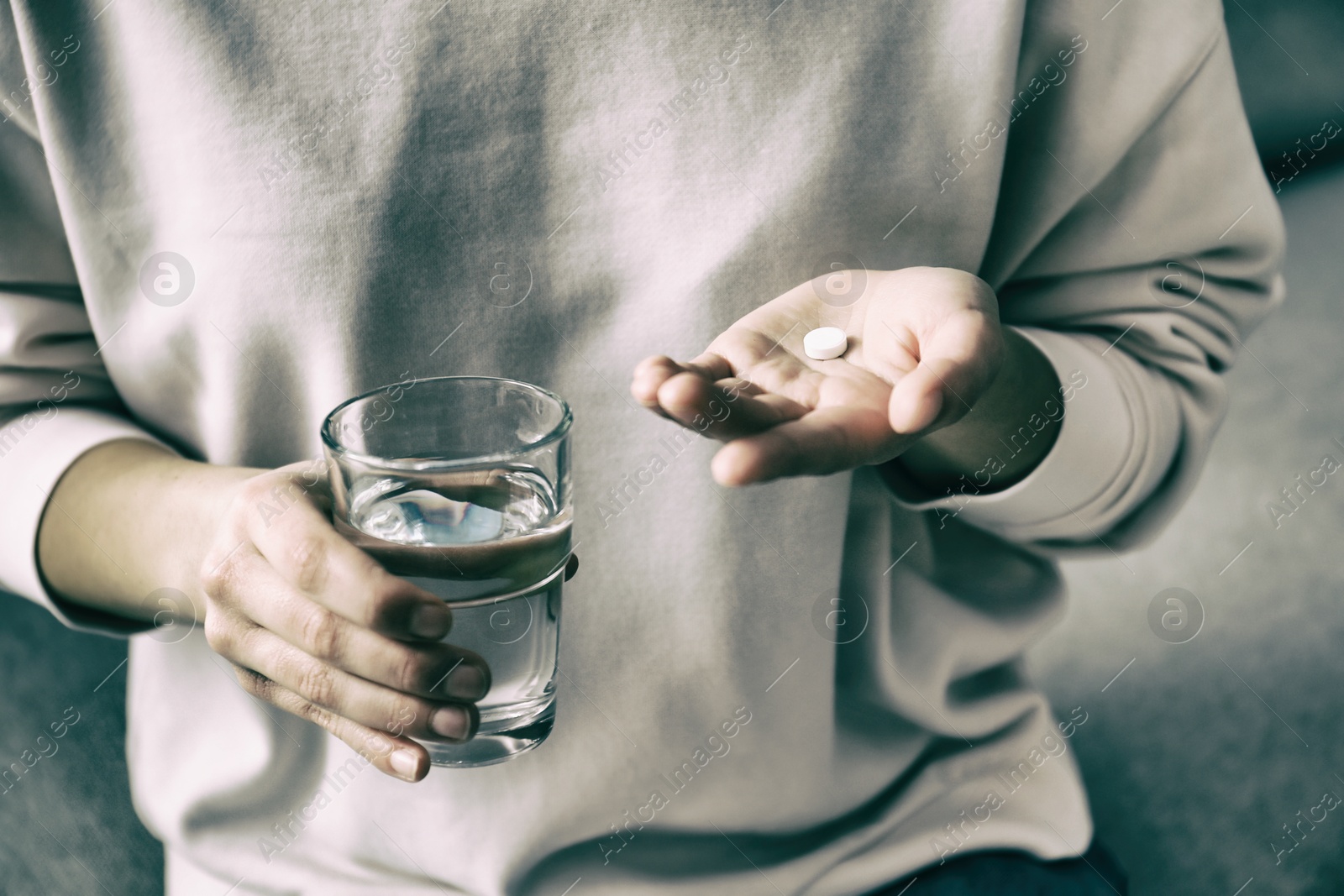 Image of Young woman with pill and glass of water indoors, closeup. Toned for dramatic atmosphere