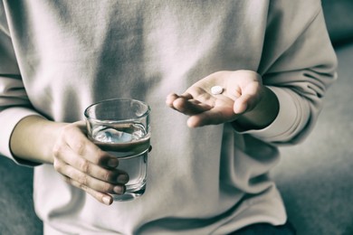 Image of Young woman with pill and glass of water indoors, closeup. Toned for dramatic atmosphere