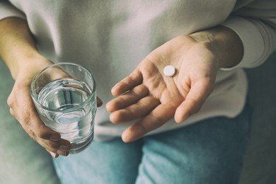 Young woman with pill and glass of water indoors, closeup. Toned for dramatic atmosphere