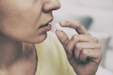 Image of Young woman taking pill indoors, closeup. Toned for dramatic atmosphere