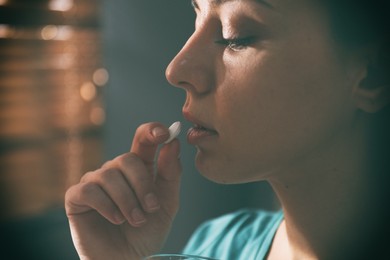 Image of Sad young woman taking pill indoors, closeup. Toned for dramatic atmosphere