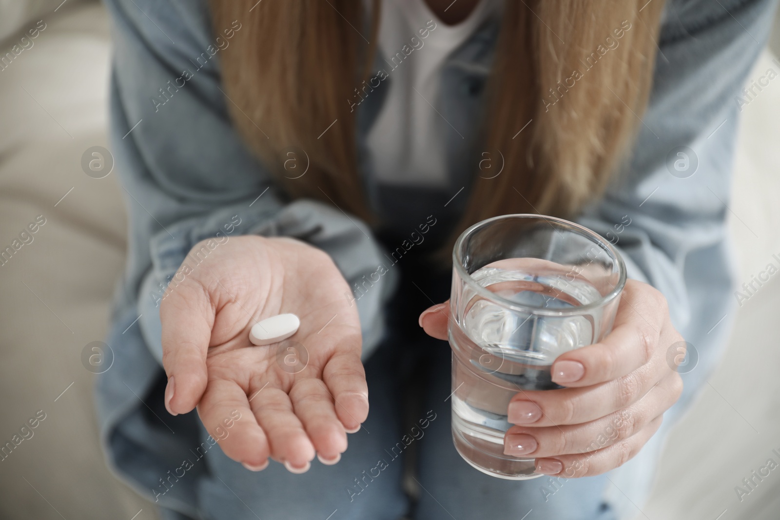 Image of Young woman with pill and glass of water indoors, closeup. Toned for dramatic atmosphere