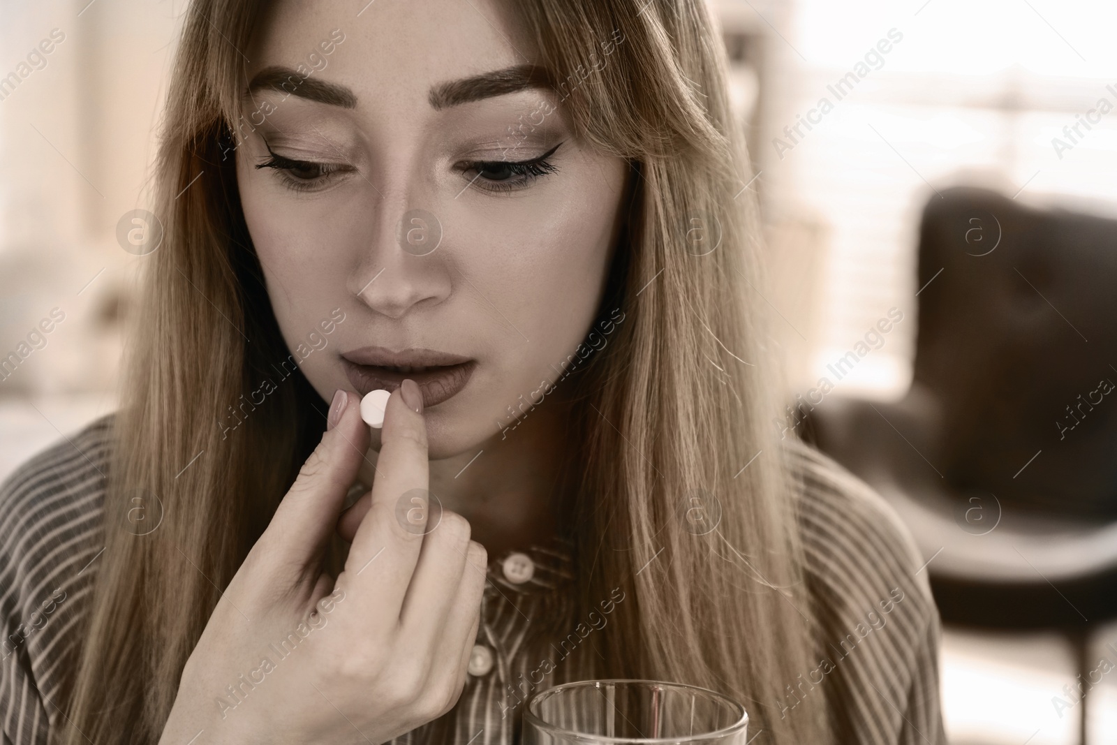 Image of Sad young woman taking pill indoors, closeup. Toned for dramatic atmosphere