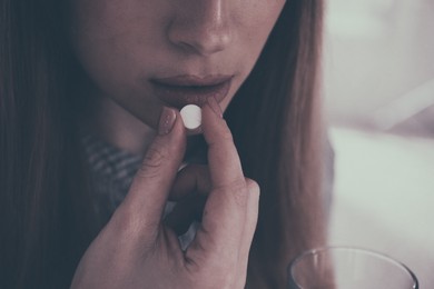 Image of Young woman taking pill indoors, closeup. Toned for dramatic atmosphere