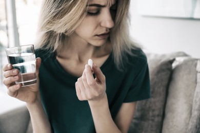 Image of Sad young woman with pill and glass of water indoors, closeup. Toned for dramatic atmosphere