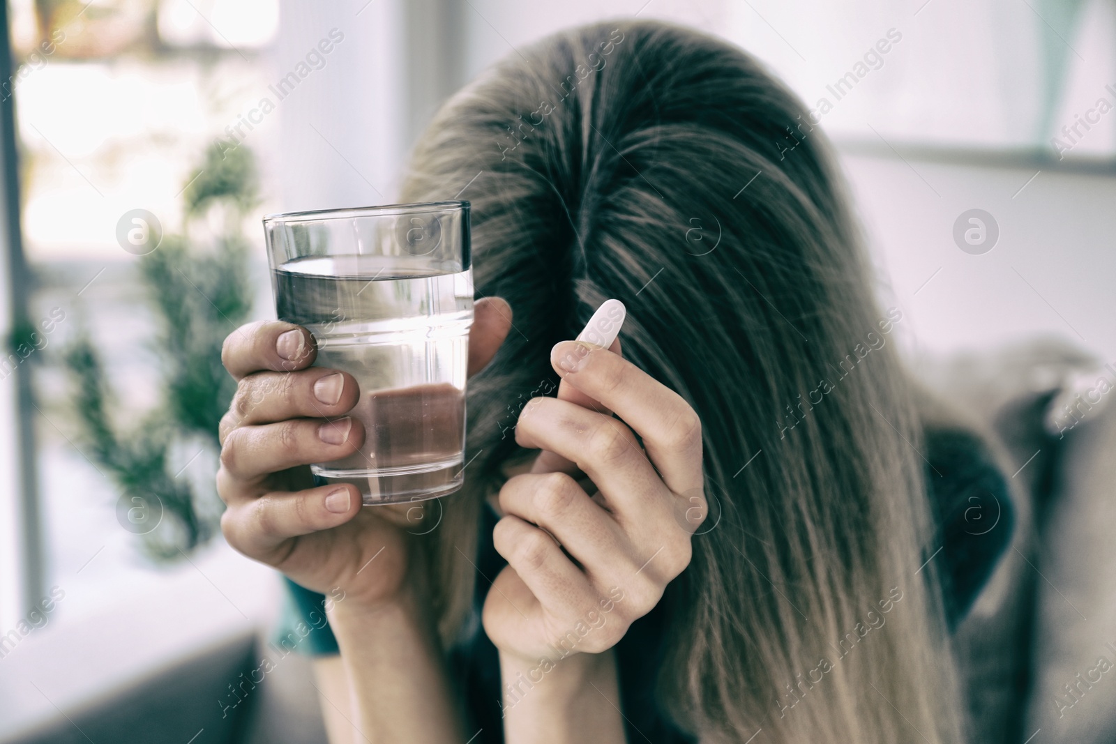 Image of Sad young woman with pill and glass of water indoors, closeup. Toned for dramatic atmosphere