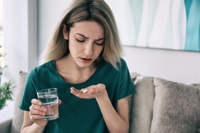 Sad young woman taking pill indoors. Toned for dramatic atmosphere