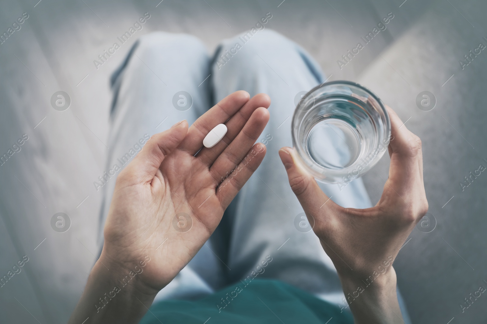 Image of Young woman with pill and glass of water indoors, top view. Toned for dramatic atmosphere