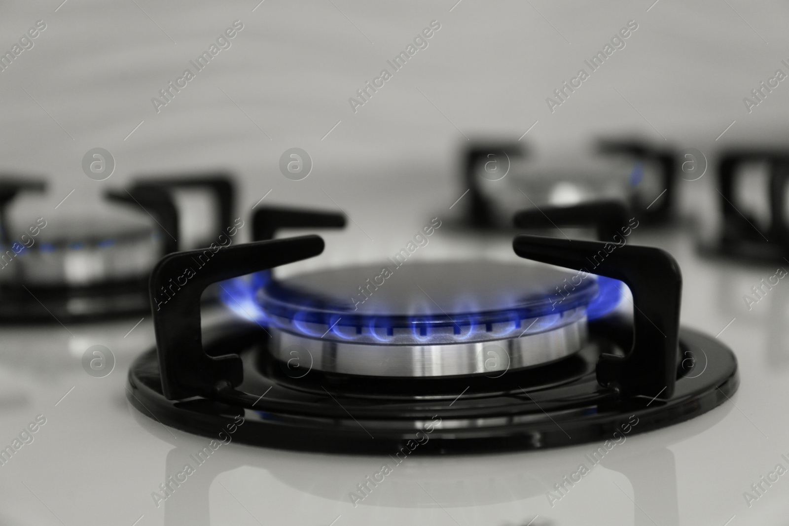 Photo of Gas burner of modern stove with burning blue flame, closeup